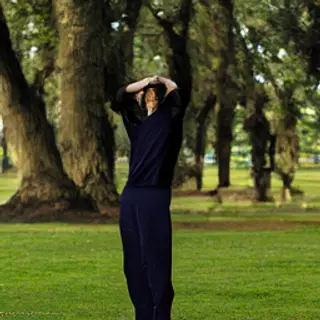 A person standing in a neutral pose in a park, full body vis