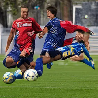 Two soccer players mid-tackle, one sliding and the other jum