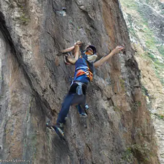 A rock climber clinging to a cliff face with arms and legs e