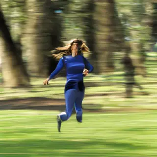 A woman mid-stride running through a park, hair and clothes 