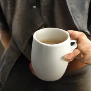 A person holding a white ceramic coffee mug by the handle wi