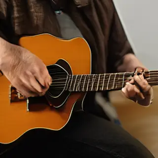 A person playing an acoustic guitar with left hand on the fr