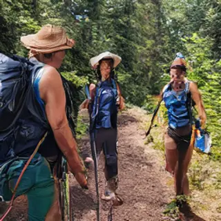 Three hikers on a trail: a man with a backpack and sunhat, a