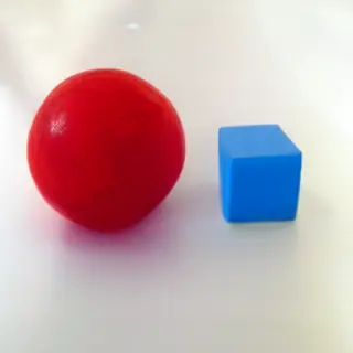 A red ball and a blue cube sitting side by side on a white s