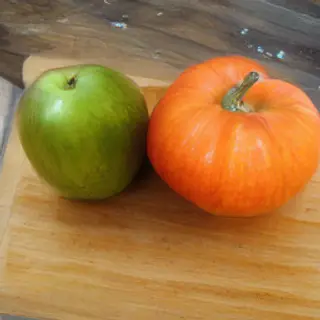 A green apple and an orange pumpkin on a wooden cutting boar