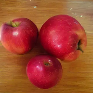 Exactly 3 red apples arranged on a wooden table