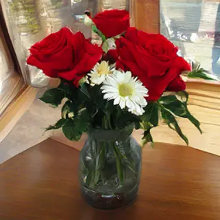 4 red roses and 2 white daisies in a glass vase on a table