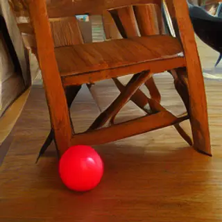 A red ball underneath a wooden chair