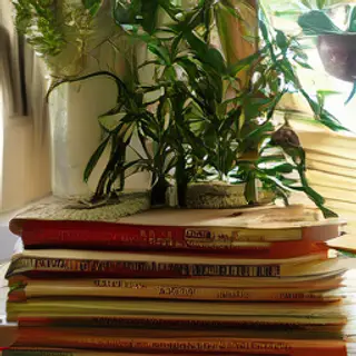 A candle on top of a stack of books, the books next to a pot
