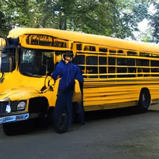 A person standing next to a yellow school bus, showing reali