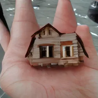 A miniature house sitting on the palm of someone's hand