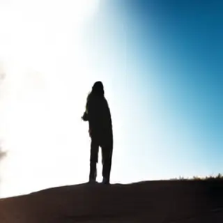 A person standing outdoors at midday with a short shadow dir