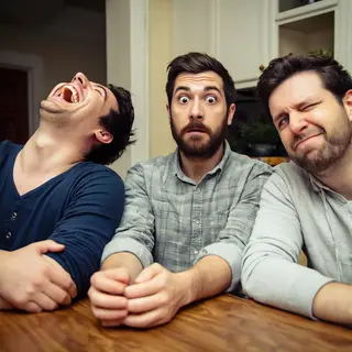 A group of three friends at a table: one laughing with head 