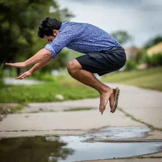 A man captured mid-jump over a puddle, body in the air with 