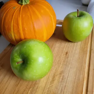 A green apple and an orange pumpkin on a wooden cutting boar