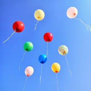 Exactly 11 colorful balloons floating against a clear blue s