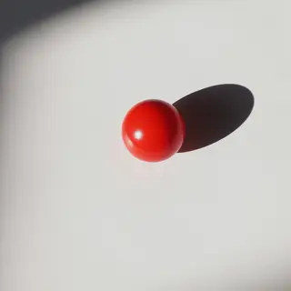 A red sphere on a white surface with a single shadow cast to