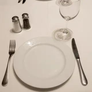 A dinner table scene with a plate, fork, knife, wine glass, 