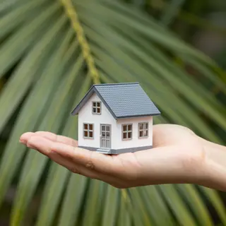 A miniature house sitting on the palm of someone's hand