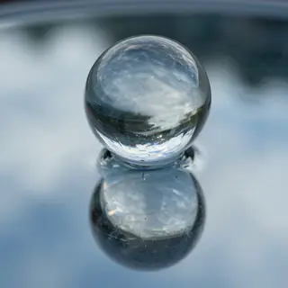 A clear glass sphere sitting on a mirror surface near a pool