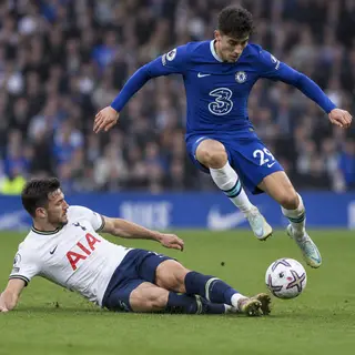 Two soccer players mid-tackle, one sliding and the other jum