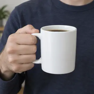 A person holding a white ceramic coffee mug by the handle wi