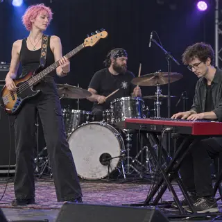 Three musicians on stage: a tall woman with short pink hair 