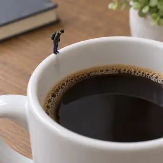 A tiny person standing on the rim of a coffee cup, looking d