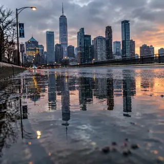 A city skyline reflected in a rain puddle on a street, with 