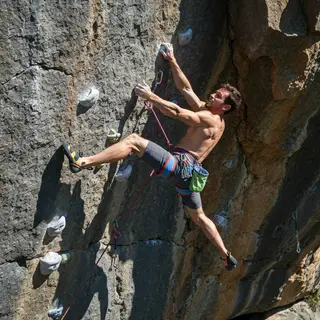 A rock climber clinging to a cliff face with arms and legs e