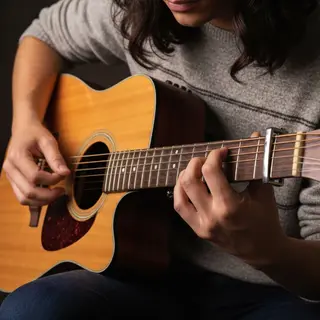 A person playing an acoustic guitar with left hand on the fr