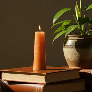 A candle on top of a stack of books, the books next to a pot