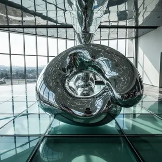 A chrome sculpture in a room with a glass floor and large wi