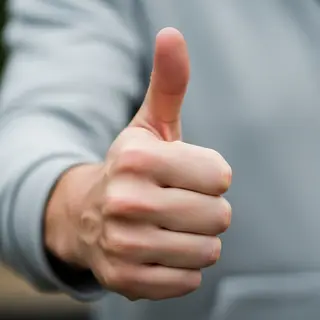 A hand giving a thumbs-up with four fingers curled and thumb