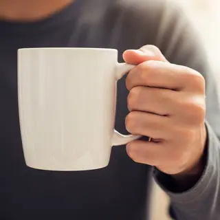 A person holding a white ceramic coffee mug by the handle wi