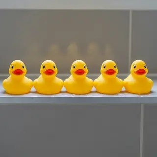 Exactly 5 yellow rubber ducks sitting in a row on a bathroom