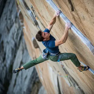 A rock climber clinging to a cliff face with arms and legs e