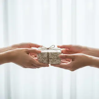One person handing a small gift box to another person, both 