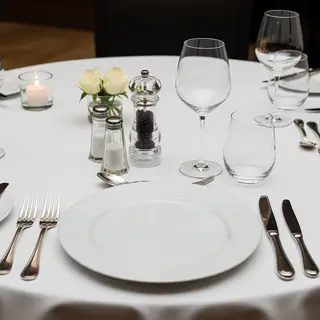 A dinner table scene with a plate, fork, knife, wine glass, 