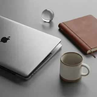 A workspace desk with a brushed aluminum laptop, a leather-b