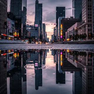 A city skyline reflected in a rain puddle on a street, with 