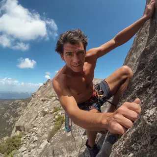 A rock climber clinging to a cliff face with arms and legs e