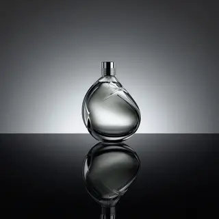 A clear glass perfume bottle on a reflective black surface w