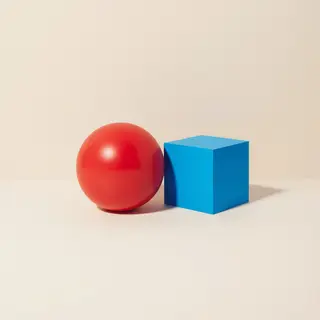 A red ball and a blue cube sitting side by side on a white s