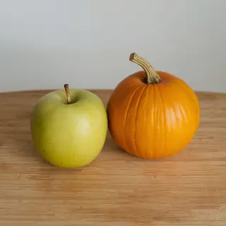 A green apple and an orange pumpkin on a wooden cutting boar