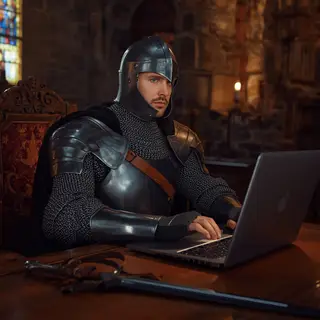 A medieval knight in full armor sitting at a desk typing on 