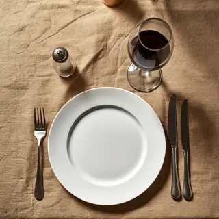 A dinner table scene with a plate, fork, knife, wine glass, 