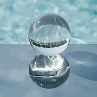 A clear glass sphere sitting on a mirror surface near a pool