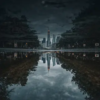 A city skyline reflected in a rain puddle on a street, with 