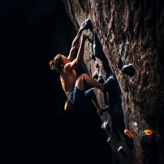 A rock climber clinging to a cliff face with arms and legs e